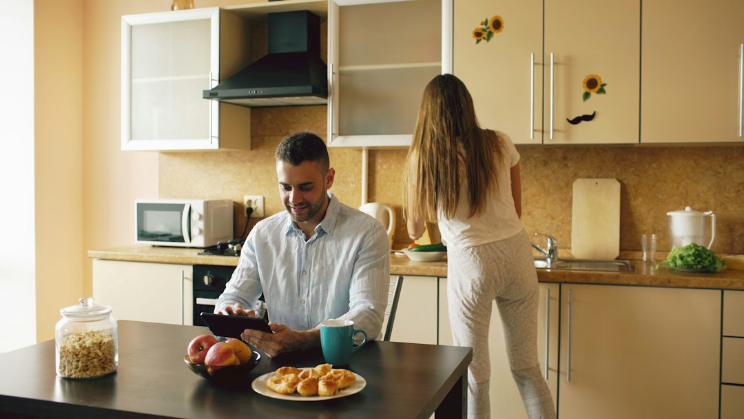 Couple in kitchen, man using tablet, woman preparing food